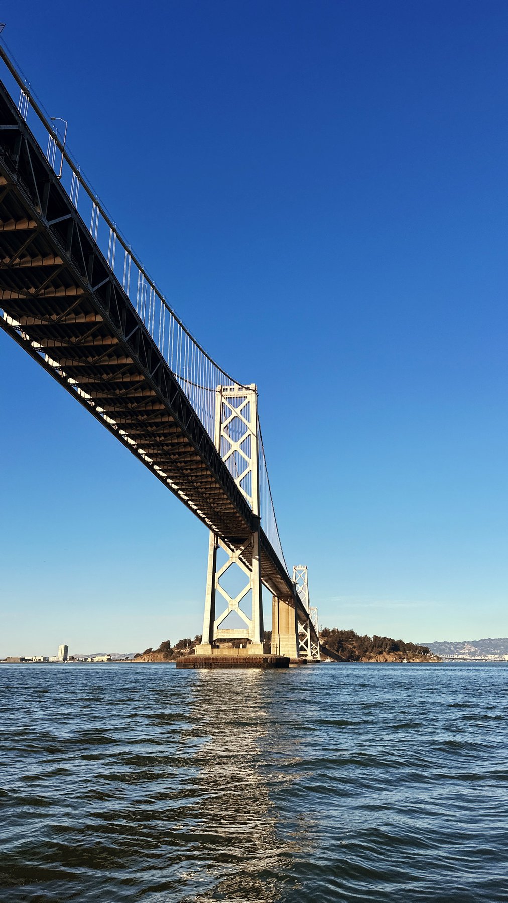 the bay bridge from below, a steep diagonal against blue sky