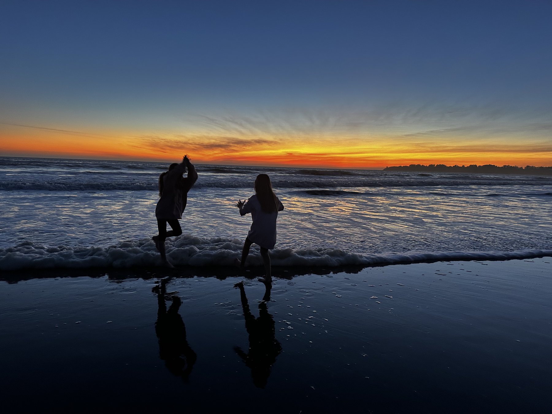 a silhouetted couple walking on wet sand at dusk