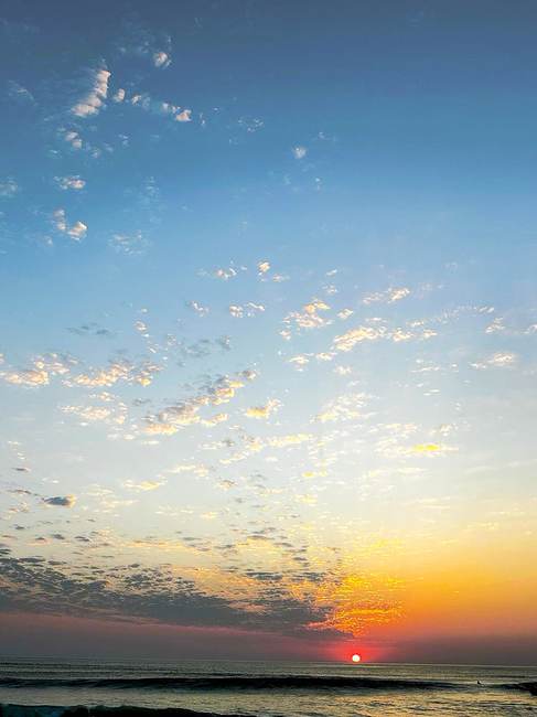 vertical sunset with textured clouds and small sun over water
